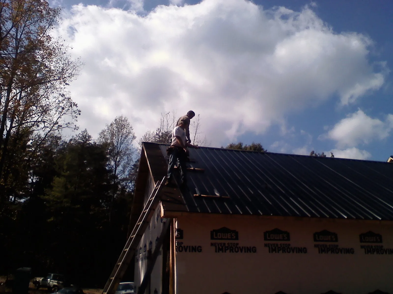 Roofer fastening dark metal panels high against a cloudy sky, from a Roof Inspection job in Mount Laguna